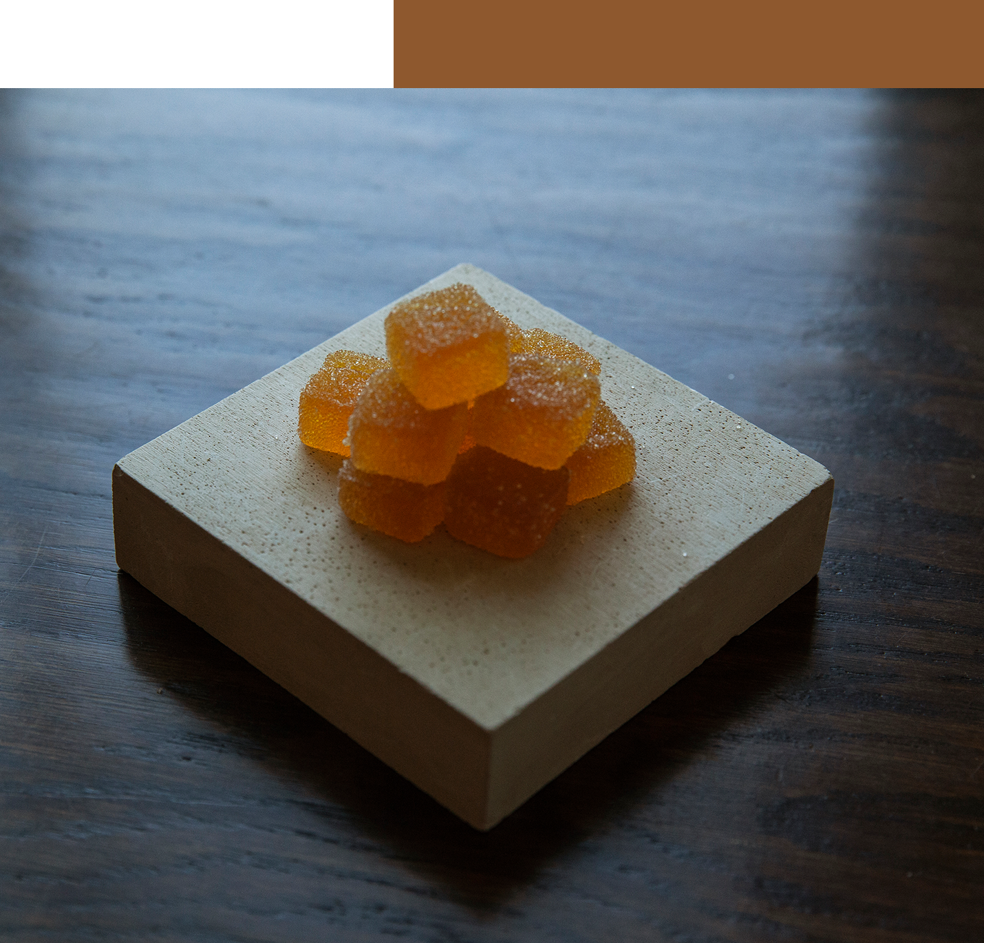 Orange gummies stacked on square stone block.