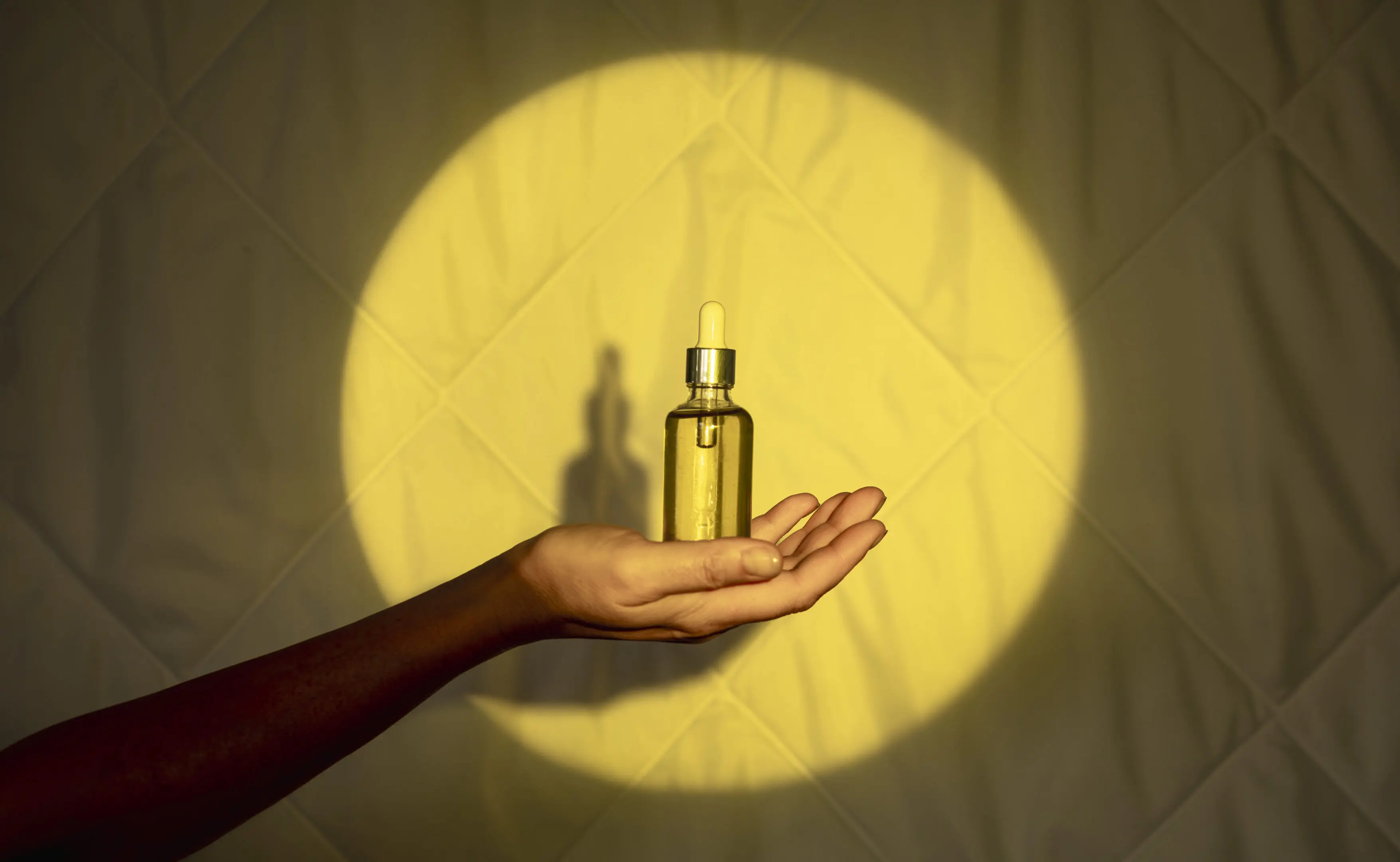 Hand holding dropper bottle in spotlight.
